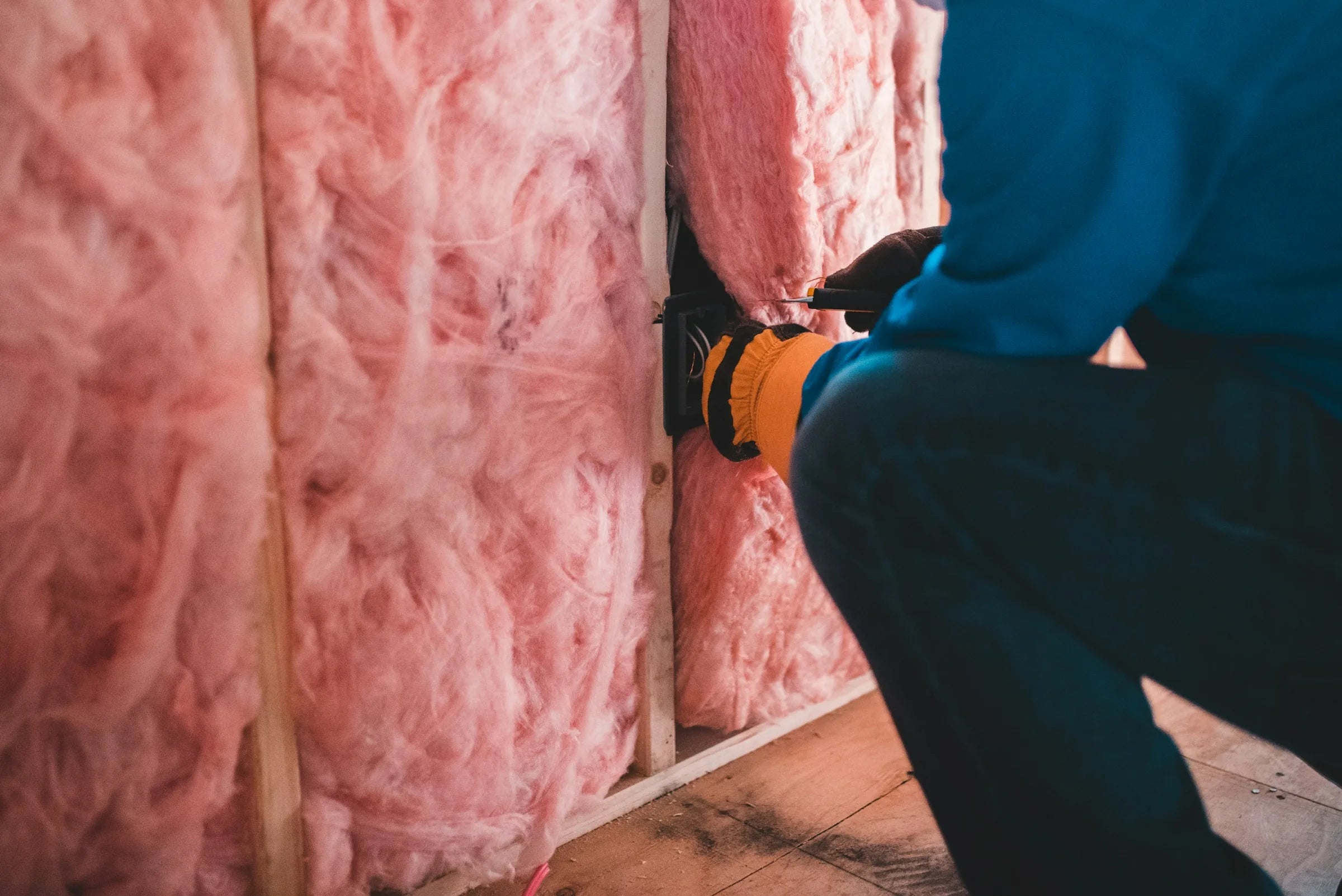 Tradesperson installing pink glass-wool insulation batts in a timber wall frame