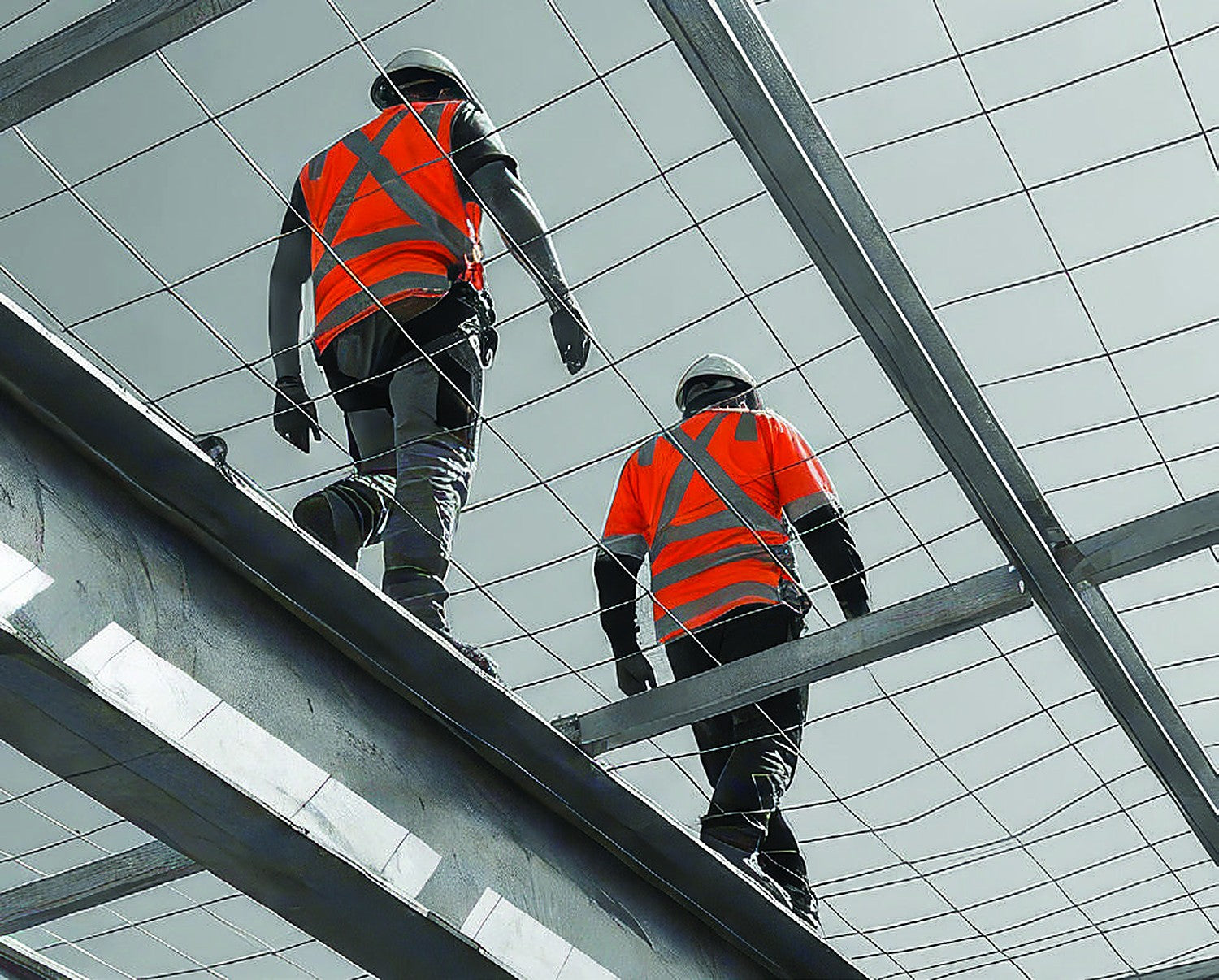 Roof safety mesh installed over steel purlins with two workers in hi-vis walking the beam above it